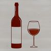 A glass containing red wine on a table with a bottle in the background.